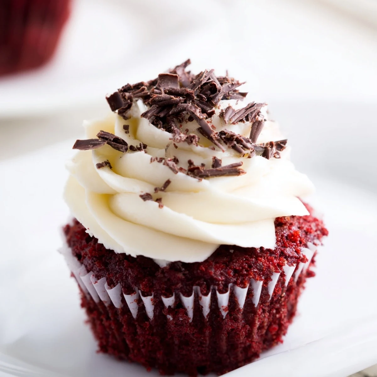 A close-up view showcases the velvety texture of Red Velvet Cupcakes with cream cheese frosting, garnished with a sprinkle of red crumbs.