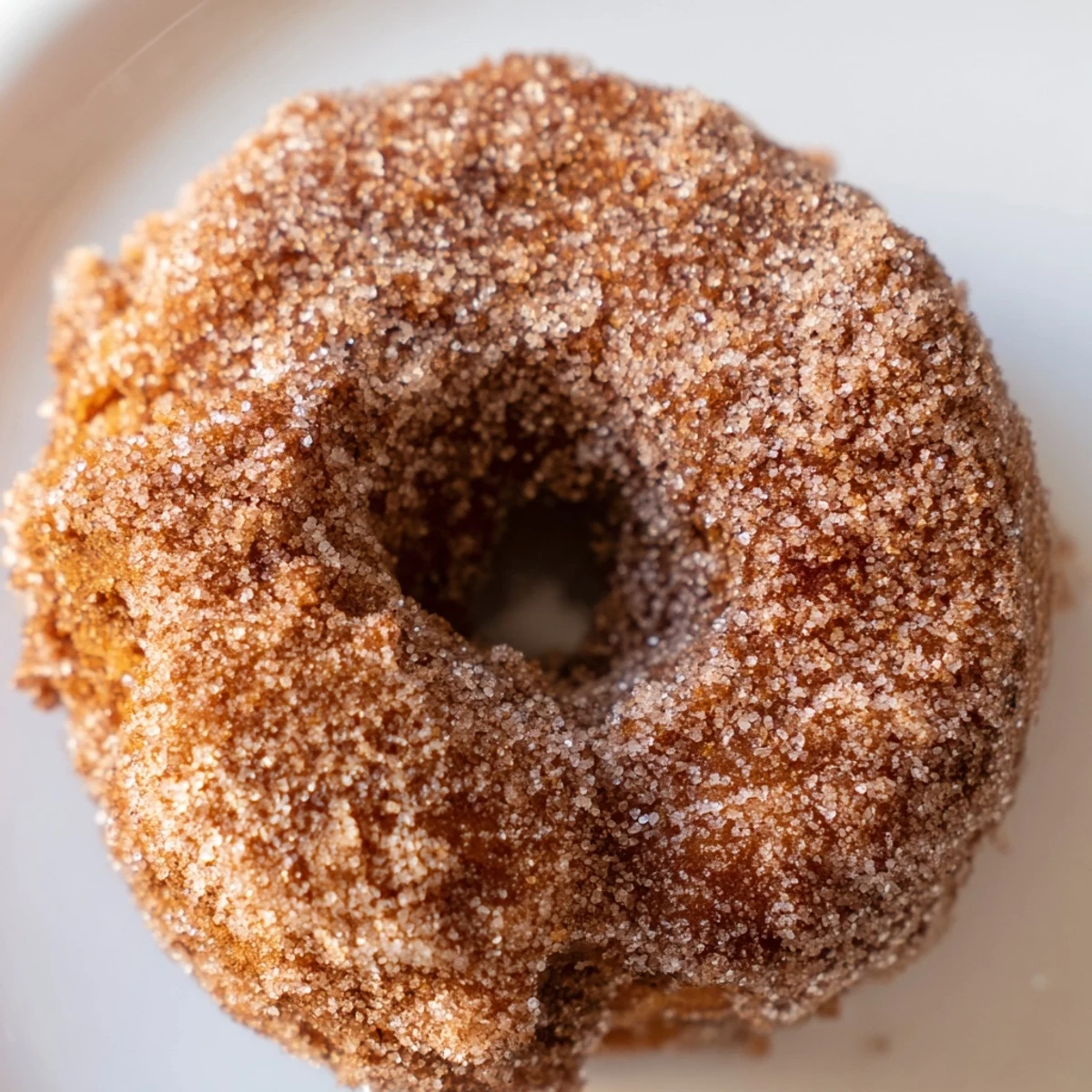 Warm Baked Apple Cider Donuts coated in sparkling cinnamon sugar, resting on a rustic wooden cutting board with fresh apple slices.