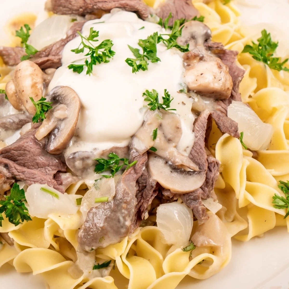 Close-up on beef stroganoff over egg noodles, with a rich, velvety mushroom sauce and a sprinkle of chopped parsley.