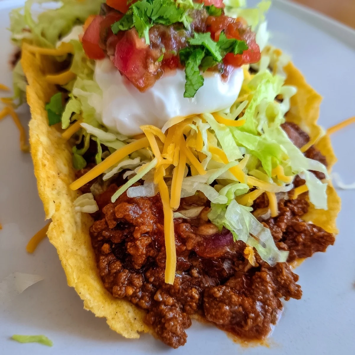 Close-up of a Beef Tacos with Hard Shells and Fresh Toppings showing juicy meat, sour cream, and vibrant diced tomatoes inside.