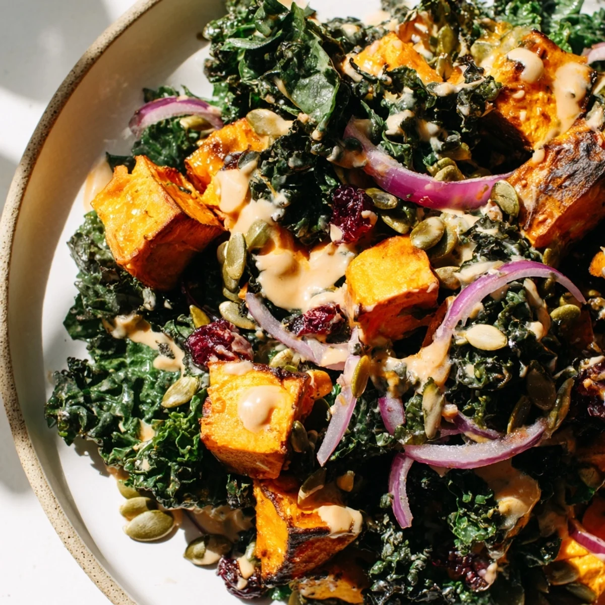 A close-up of the kale and sweet potato salad shows golden roasted vegetables, a drizzle of tahini dressing, and fresh parsley.