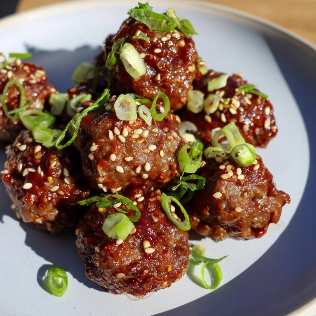 Close-up of juicy Spicy Sriracha Beef Meatballs with Sesame, showing the tender beef texture and toasted sesame seeds on a white plate.