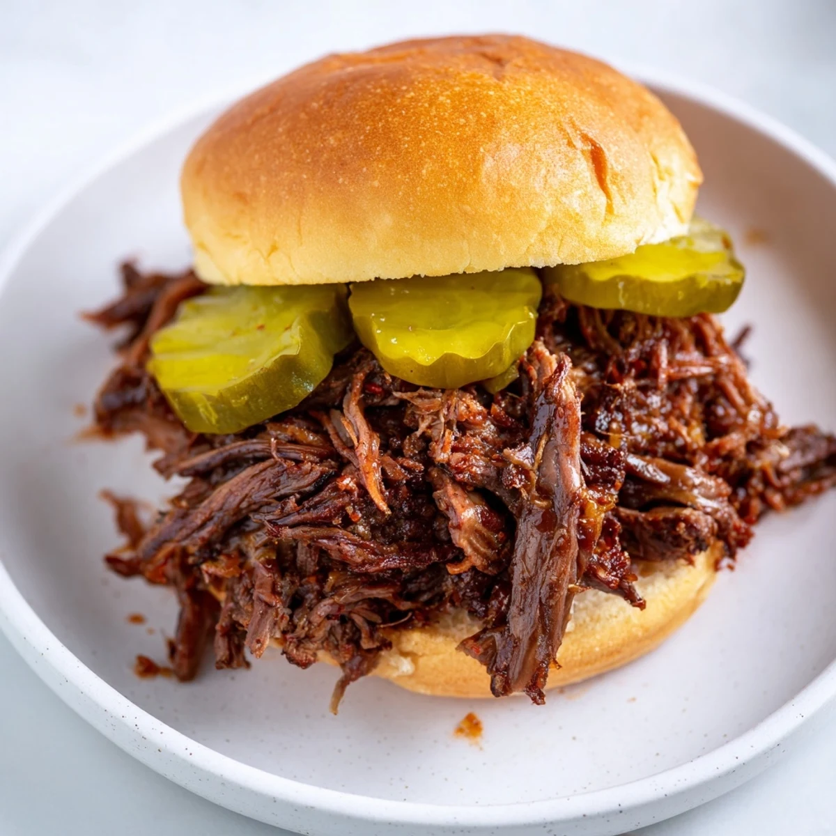 Shredded beef piled onto soft slider buns, garnished with pickles for a tangy, savory mini-sandwich bite.