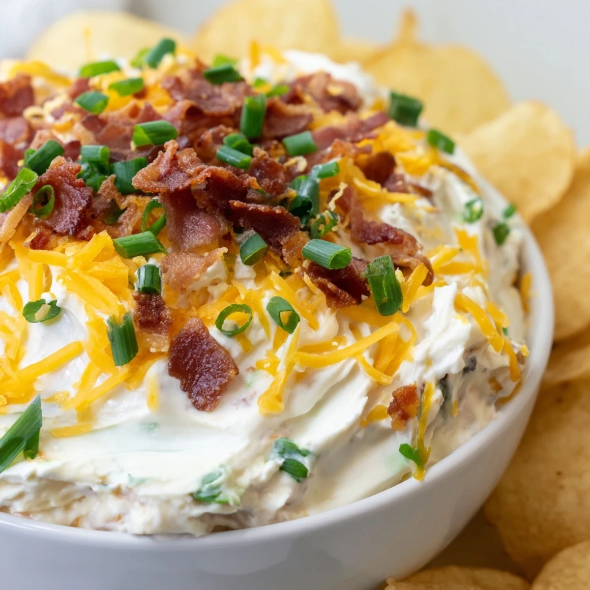 Creamy Loaded Baked Potato Dip with crisp potato chips for dipping, garnished with fresh chives and crumbled bacon.