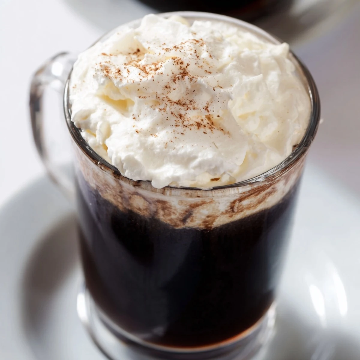 Close-up of the Irish Coffee Mocktail with Whipped Cream, highlighting the fluffy topping on rich, dark coffee in a clear glass.  