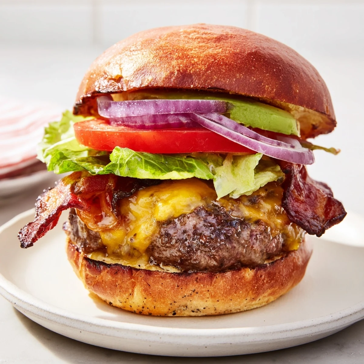 A close-up of a Beef Burger with Avocado and Beef Bacon on a toasted bun, with melted cheese and fresh lettuce visible.