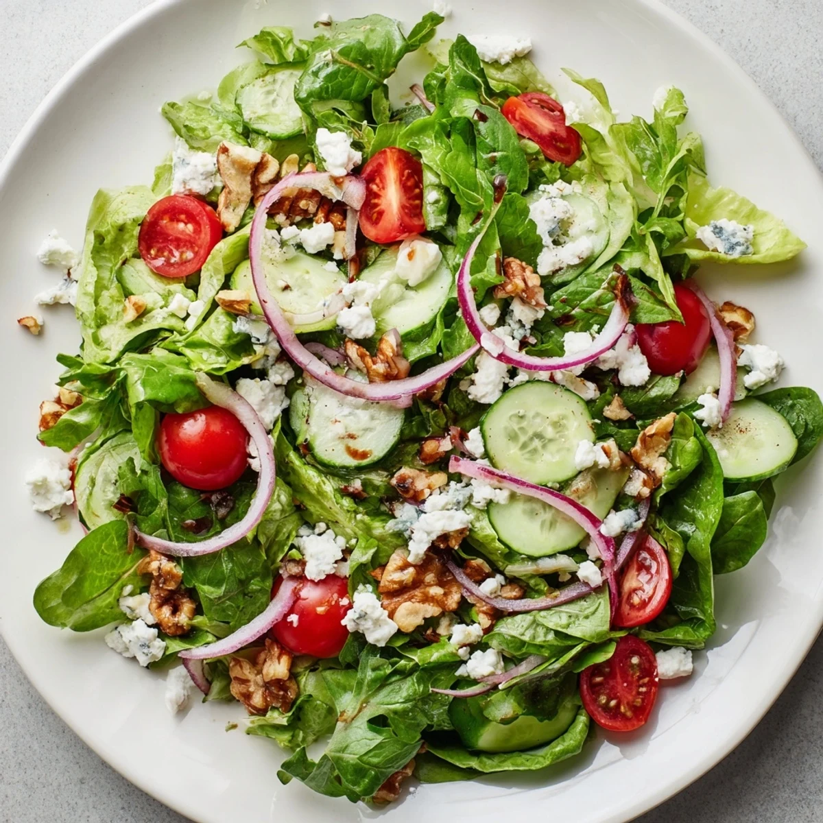 A close-up of Spring Mix Salad with Balsamic Vinaigrette featuring sliced radishes and greens glistening with tangy homemade dressing on a white plate.