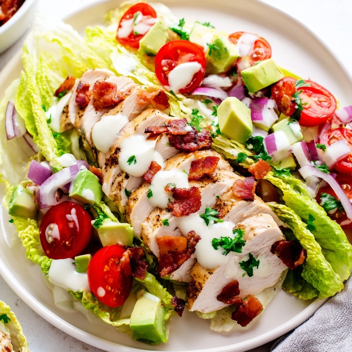 A fresh BLT Chicken Salad garnished with avocado slices and chives on a bed of chopped romaine.