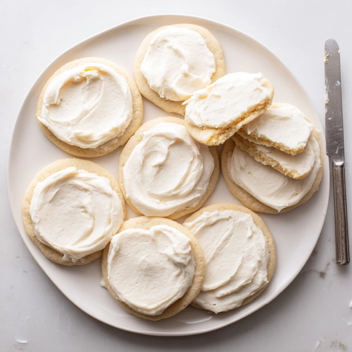 Easy Sugar Cookie Frosting is spread with a spatula over freshly baked cookies for a smooth, glossy finish.