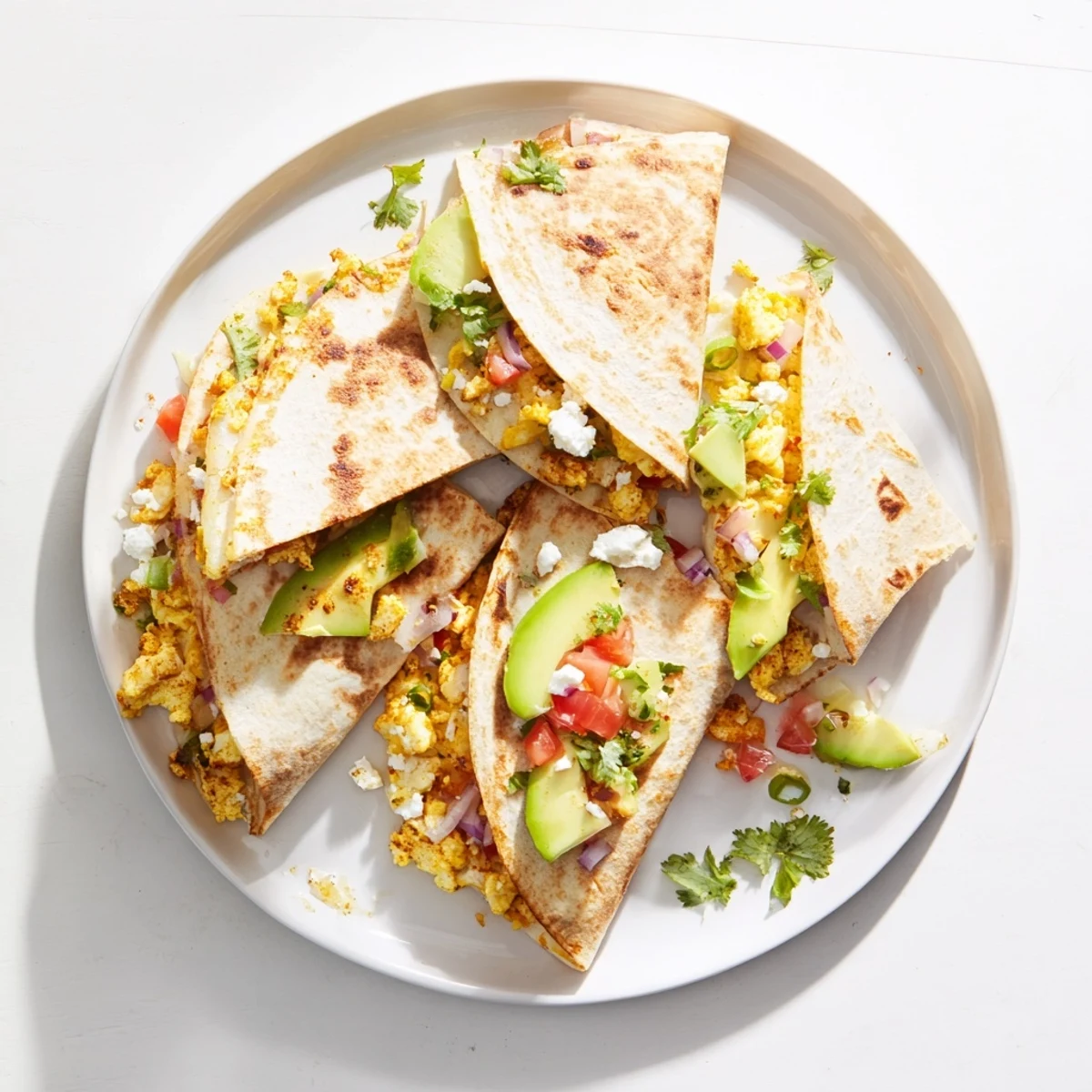 A close-up view of crispy Spicy Avocado Egg and Three Cheese Quesadillas stuffed with fluffy scrambled eggs, feta crumbles, and fresh jalapeño pieces.