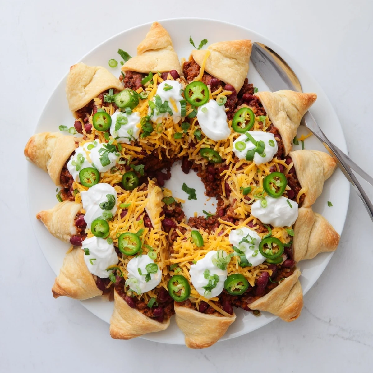 Golden-baked Beef Chili Taco Crescent Roll Ring with melted cheddar, sliced and served with sour cream and jalapeños.
