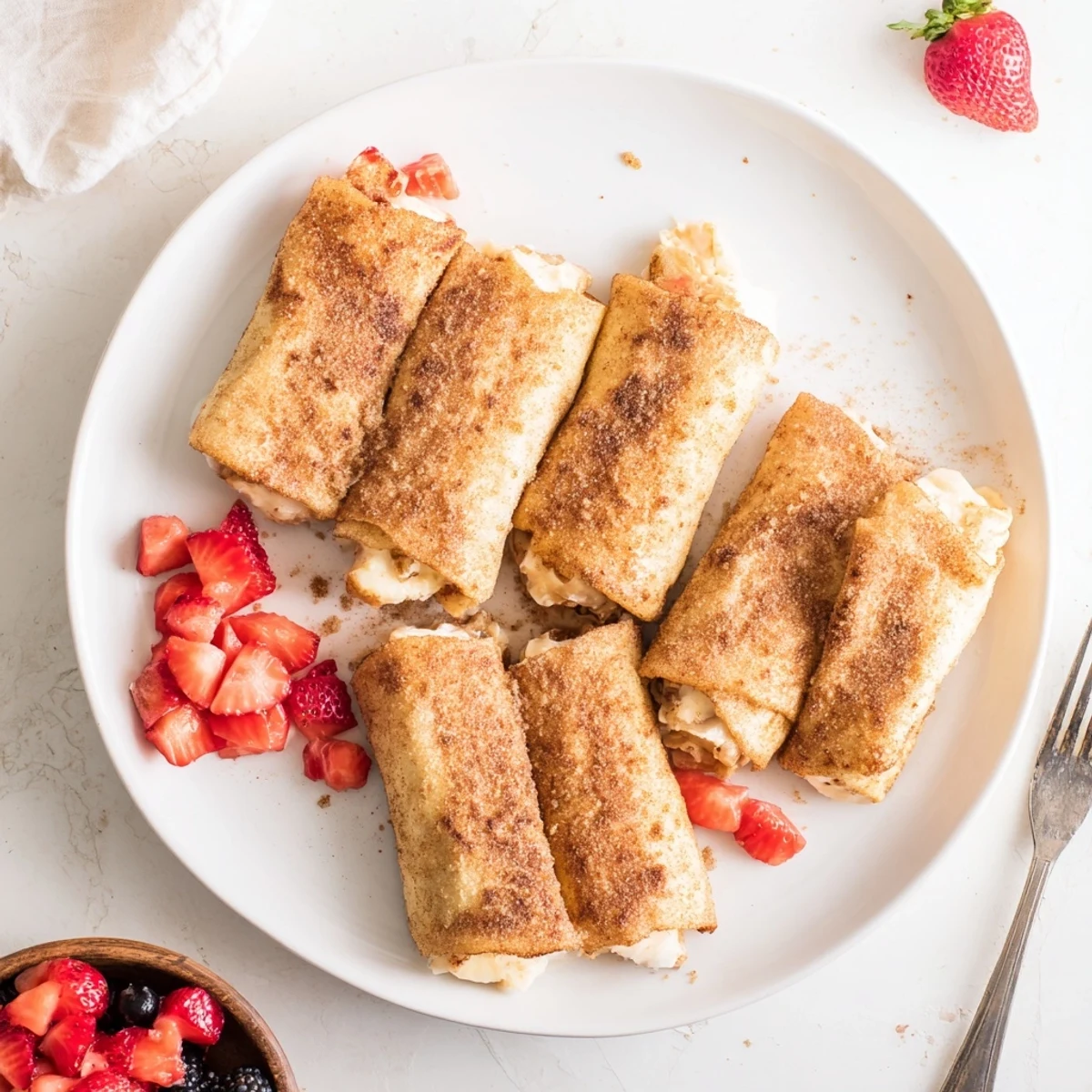A close-up of golden-brown Cheesecake Dessert Chimichangas Cinnamon Sugar Delights, dusted with sparkling sugar beside fresh berries.