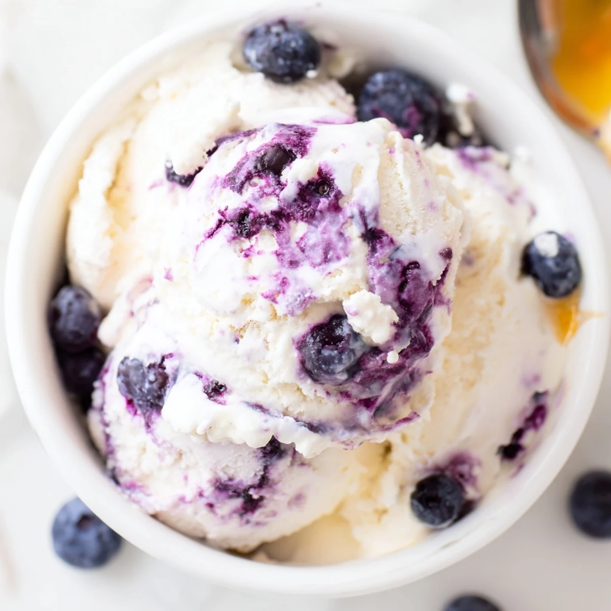 A creamy scoop of Blueberry Cottage Cheese Ice Cream served in a bowl, garnished with fresh mint and a drizzle of honey for a refreshing summer dessert.