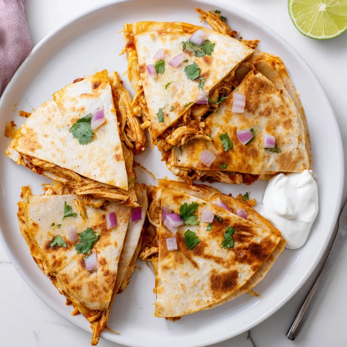 A close-up of Hot Honey BBQ Chicken Quesadillas with red onion and fresh cilantro, served beside sour cream and limes.
