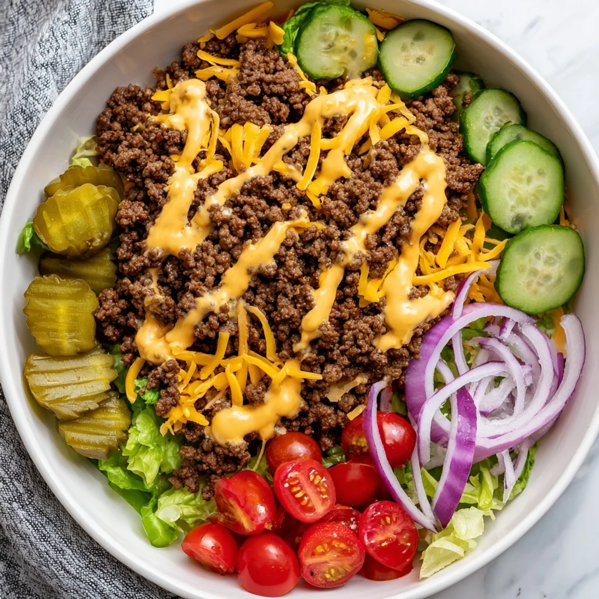 Hearty burger bowls with ground beef, cheddar, onions, and pickles are drizzled with tangy sauce for weeknight dinner.