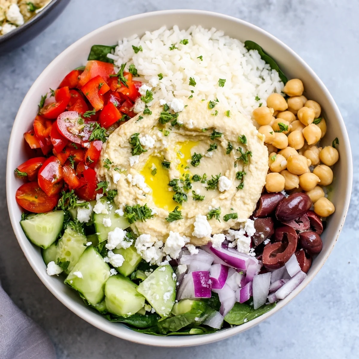 Colorful Mediterranean rice bowl with crisp vegetables, creamy hummus, and lemon-tahini drizzle in a white serving dish