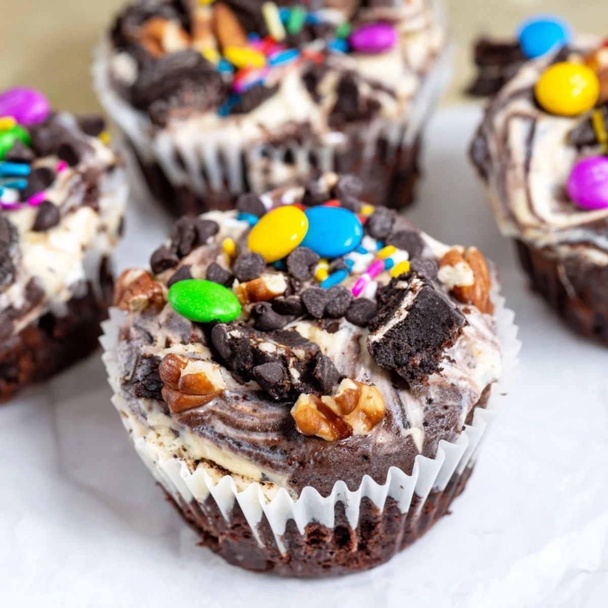 Rich loaded brownie cheesecake cups topped with colorful sprinkles and chocolate chips in a muffin tin