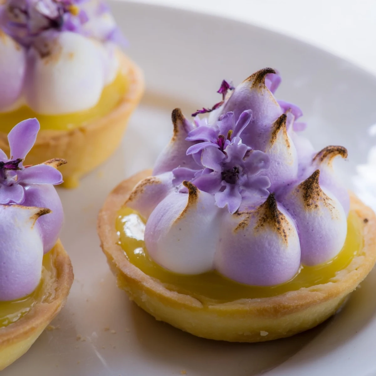 Mini lemon tart filled with tangy curd beneath fluffy lilac meringue peaks