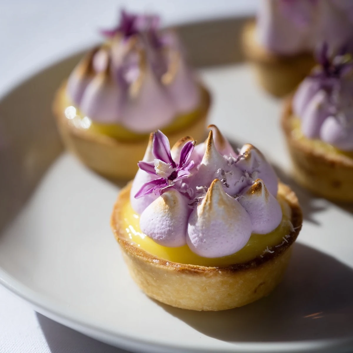 Golden mini lemon tart with lilac meringue topped on a white plate
