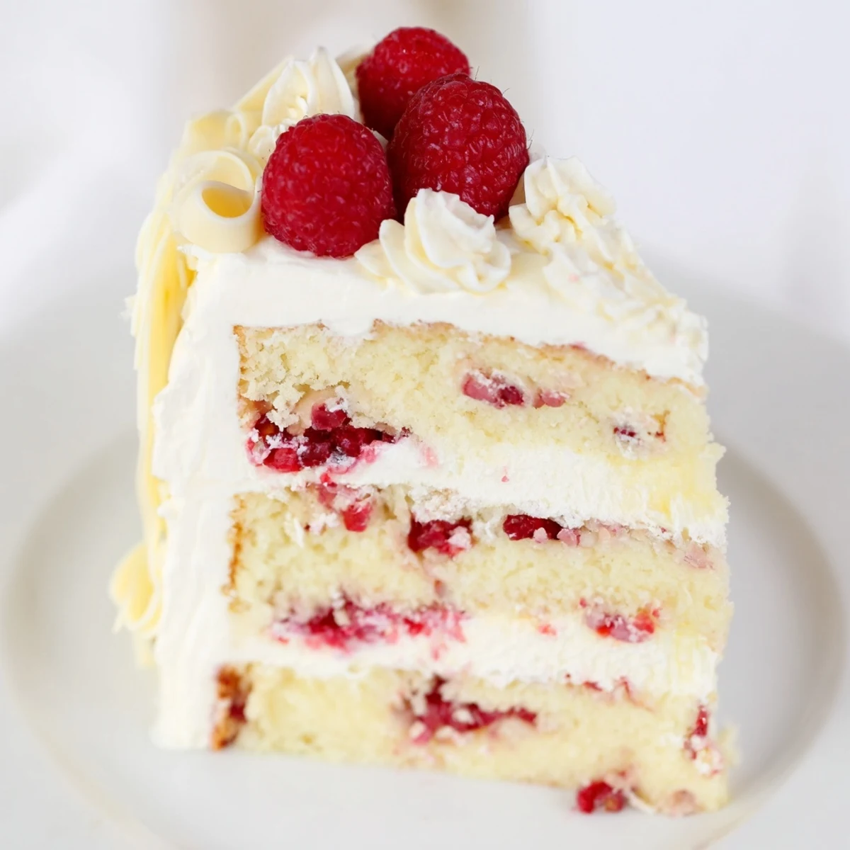 Slice of white chocolate raspberry cream cake showing layers of vanilla sponge and red raspberry filling