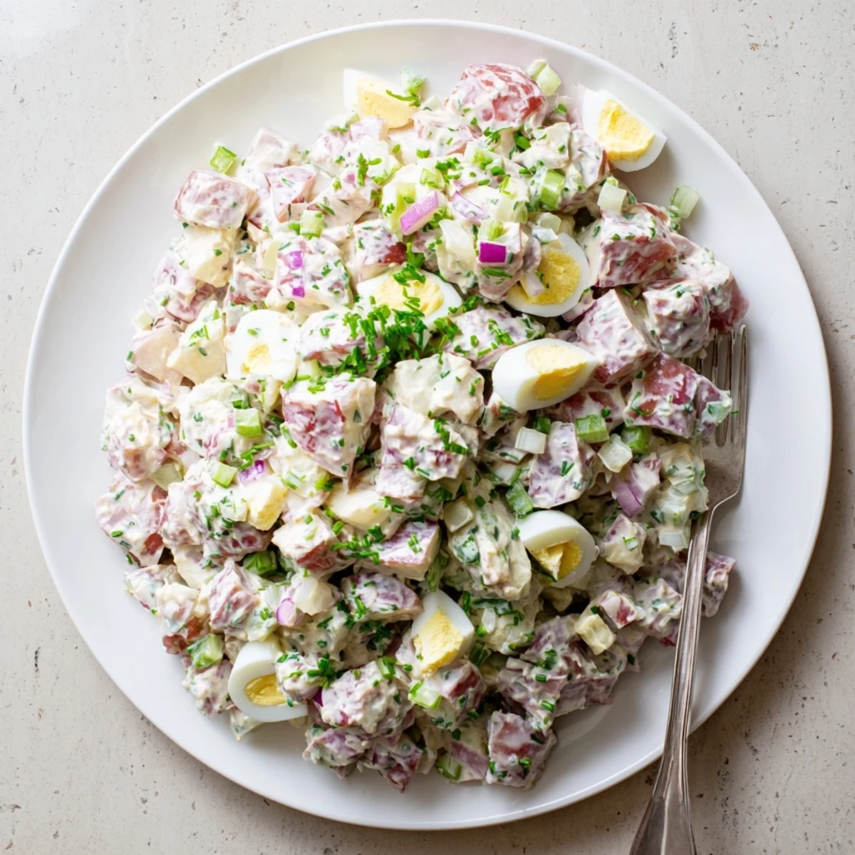 Classic American red potato salad dotted with hard-boiled eggs and chopped green chives