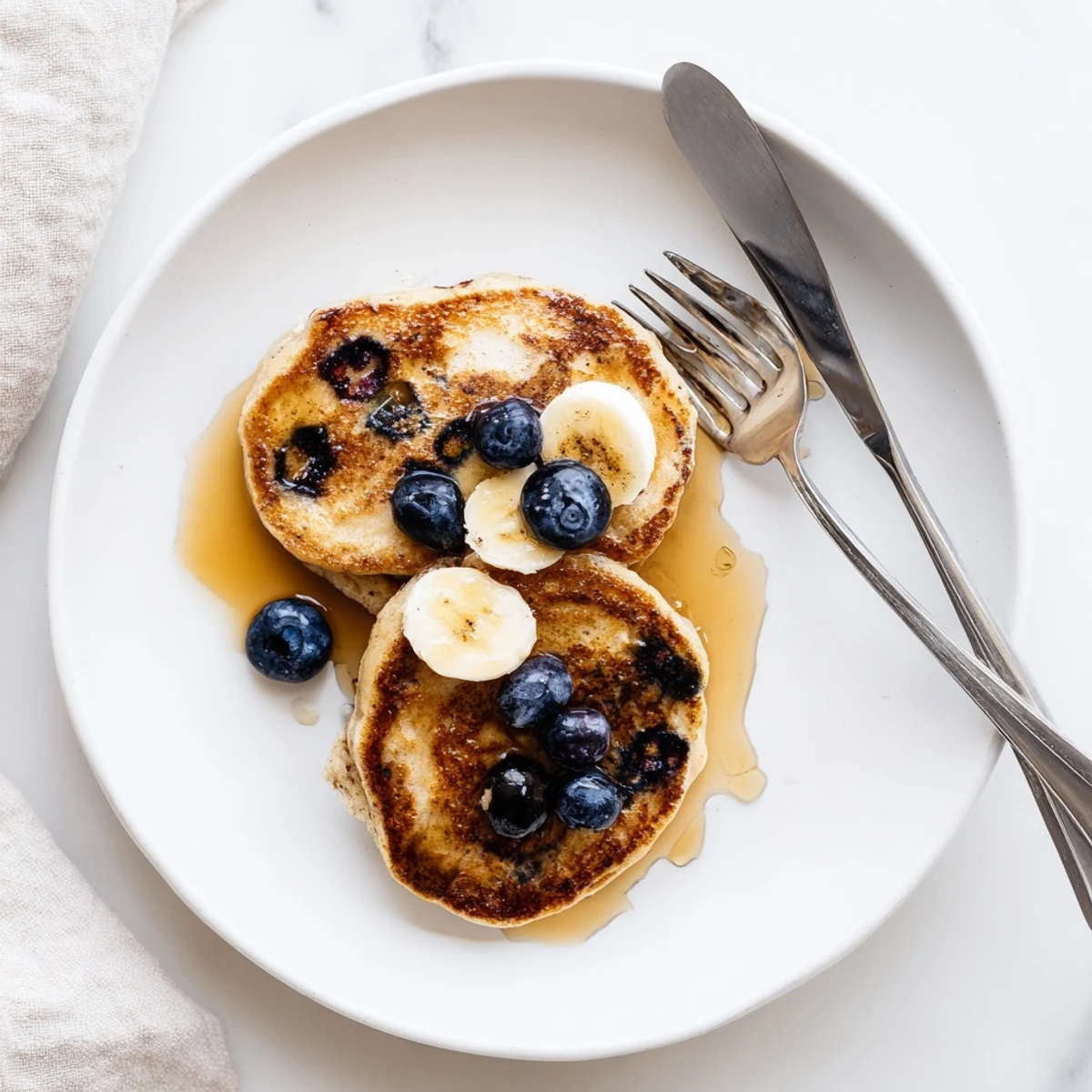 Protein-rich Greek yogurt banana pancakes topped with fresh banana slices and honey on a white plate