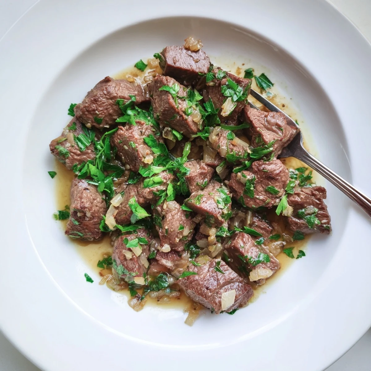 Tender Crockpot steak bites glistening with garlic butter sauce and fresh parsley garnish