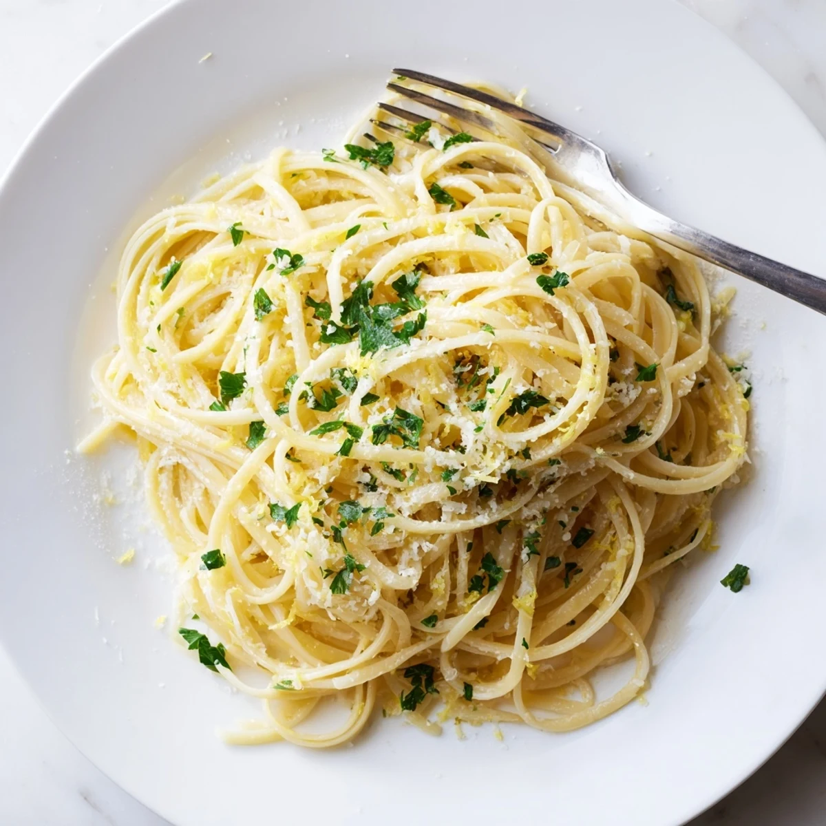 Steaming plate of garlic butter pasta twirled high with lemon zest and black pepper
