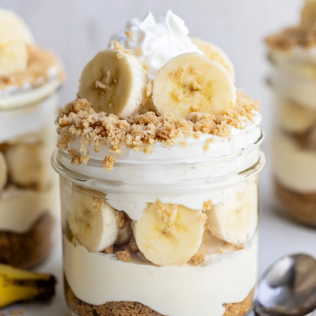 Creamy no bake banana pudding cheesecake cups topped with fresh banana slices and golden wafer crumbs