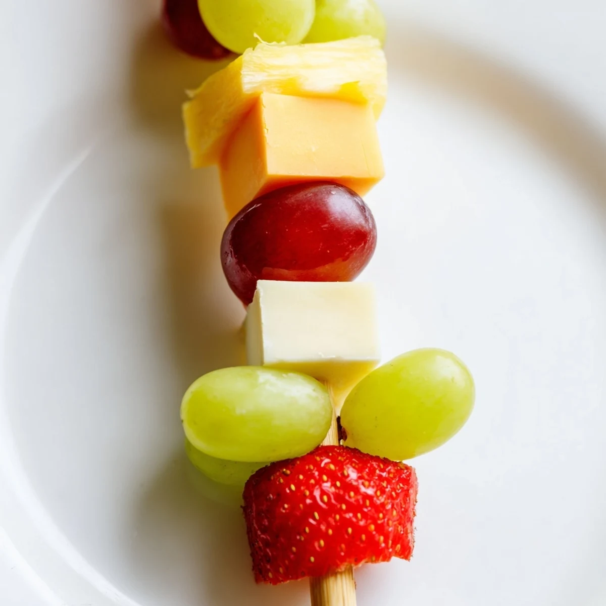 Colorful fruit and cheese kabobs arranged on a platter with grapes, strawberries, pineapple, and cheddar cubes