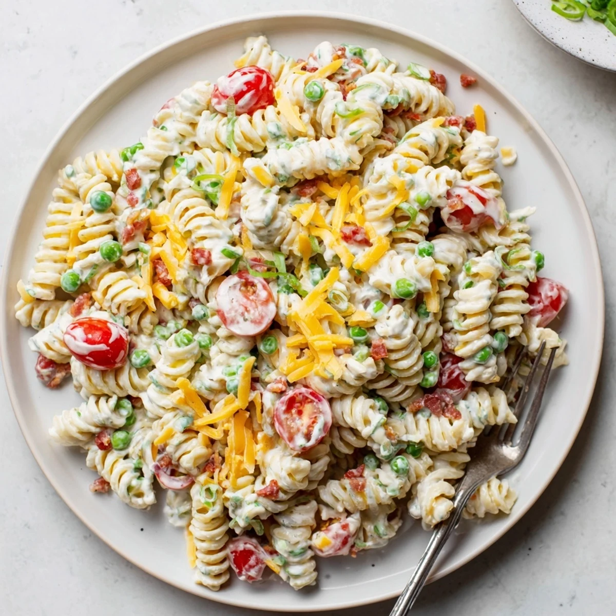 Hearty crack pasta salad topped with shredded cheddar and crispy bacon bits on a platter