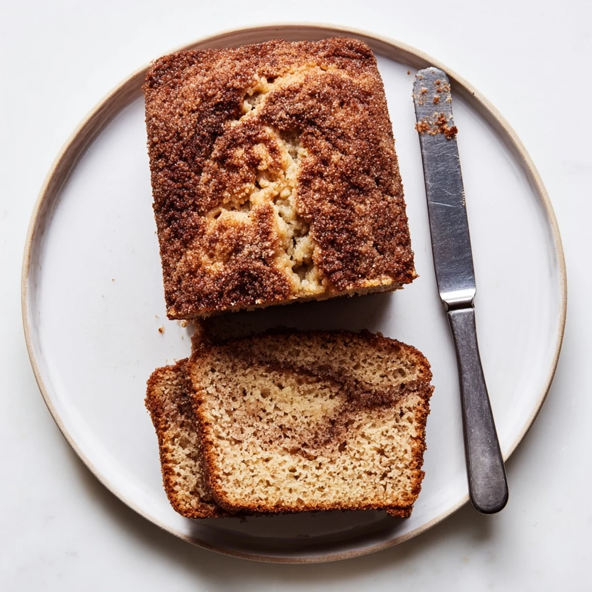 A golden slice of snickerdoodle banana bread with a marbled cinnamon-sugar swirl on a white plate.