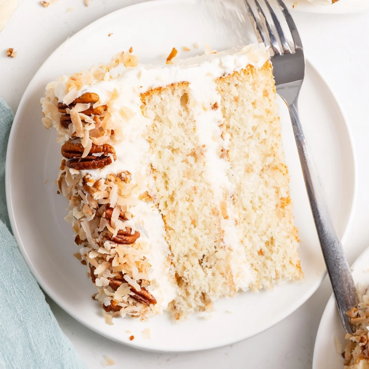 Moist Italian cream cake slice topped with creamy white frosting and toasted pecans