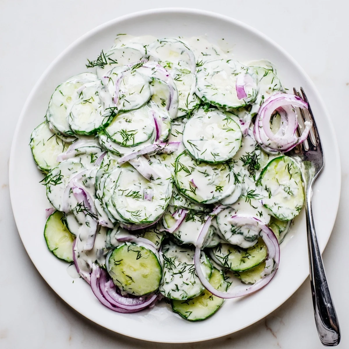 Cold cucumber dill salad served in white bowl featuring thinly sliced cucumbers red onion and creamy yogurt dressing
