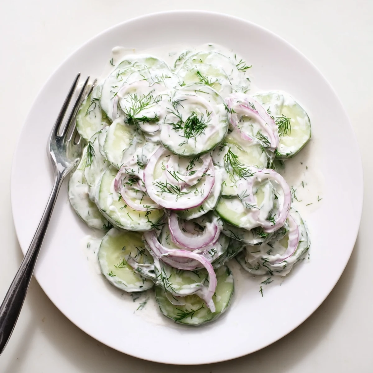 Summer side dish of cucumber dill salad with sour cream dressing fresh dill and red onion on rustic table