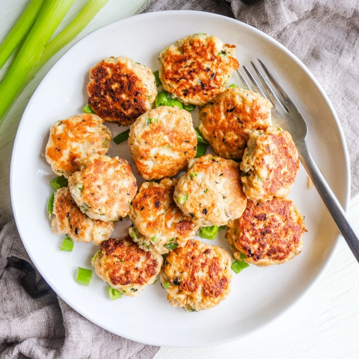 Golden brown keto cheesy chicken fritters served on a white plate with fresh green onions