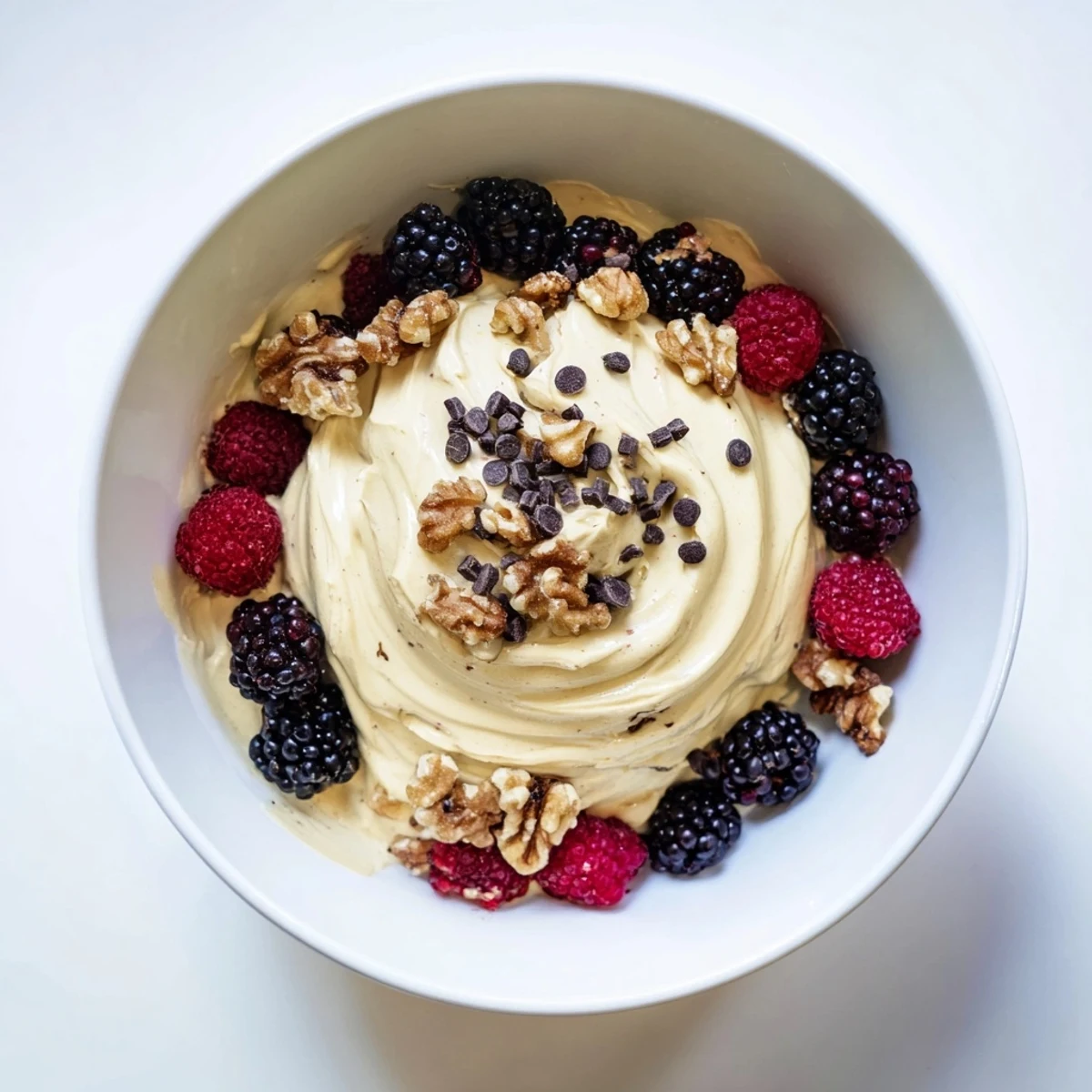 Creamy banana nice cream swirled in a glass bowl topped with fresh berries and chopped nuts