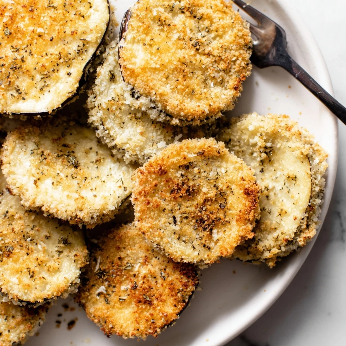 Crispy Baked Eggplant piled on a platter, crispy edges and olive oil sheen