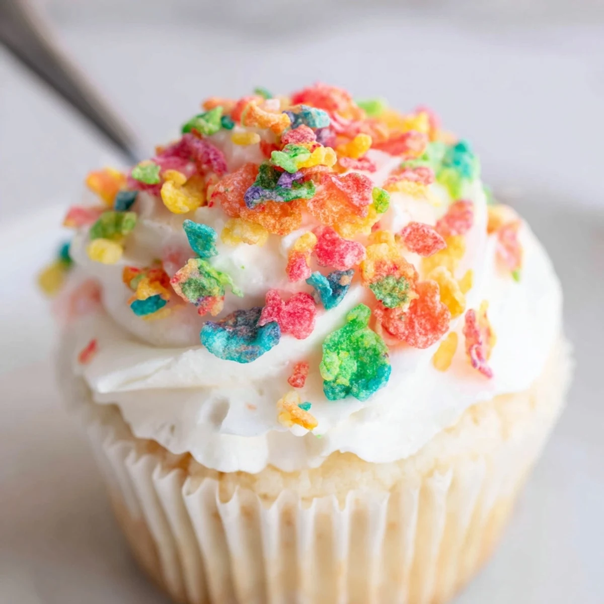 Fluffy rainbow cereal frosting in a glass bowl topped with crunchy Fruity Pebbles garnish