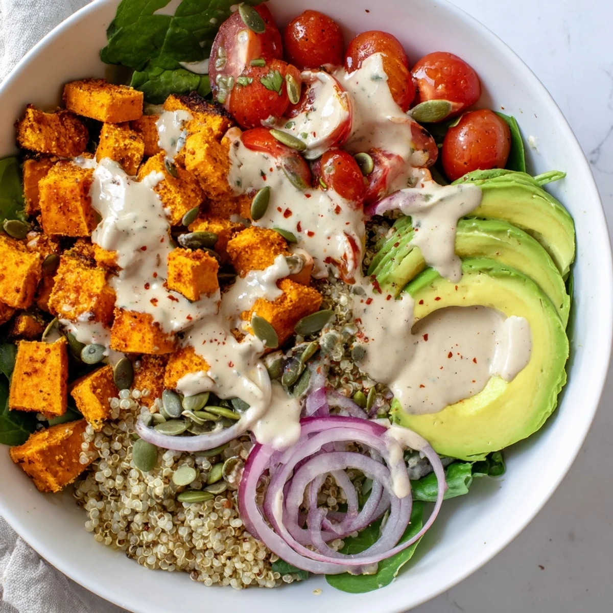 Colorful sweet potato bowl with roasted veggies, avocado, and creamy tahini dressing