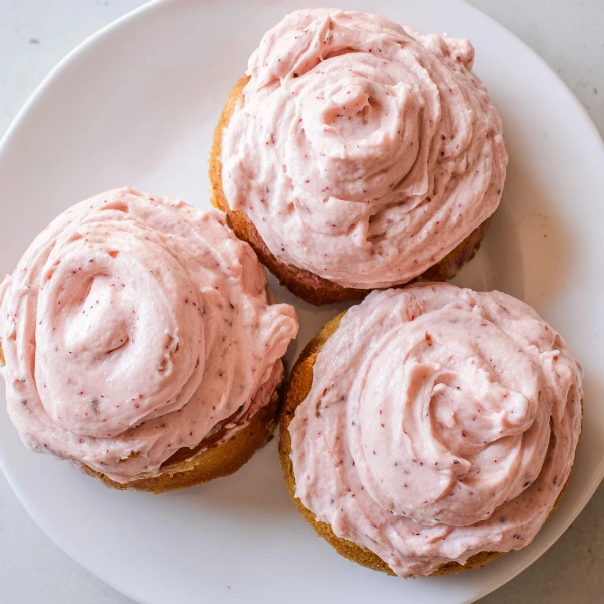 Soft baked Strawberry Buttercream Frosted Donuts with swirled pink icing on a rustic plate