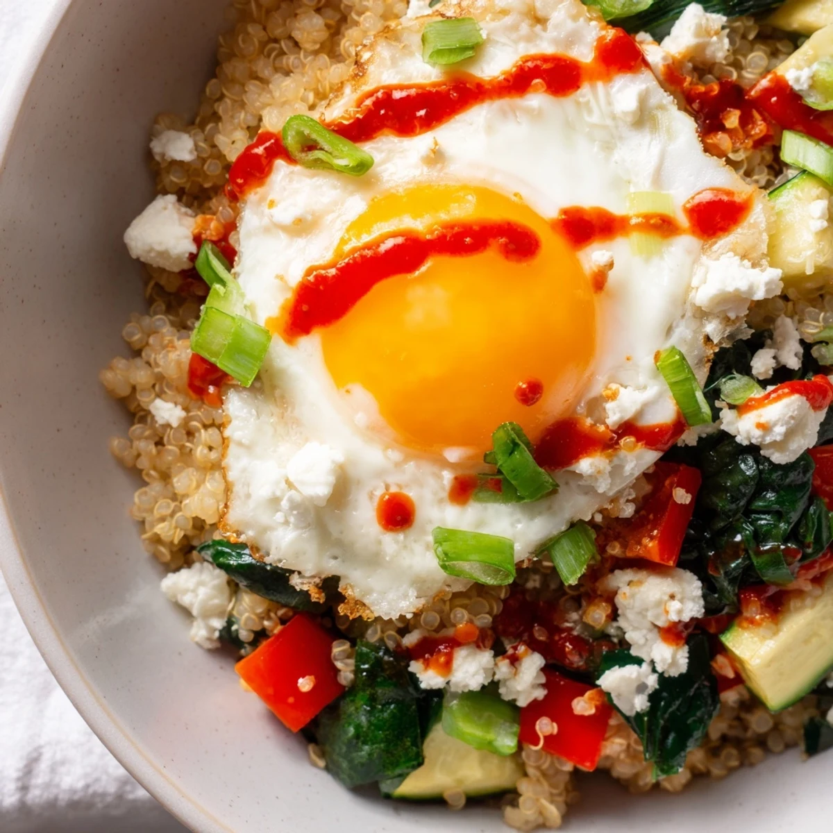 Warm savory quinoa breakfast bowl loaded with sautéed vegetables and crumbled feta cheese