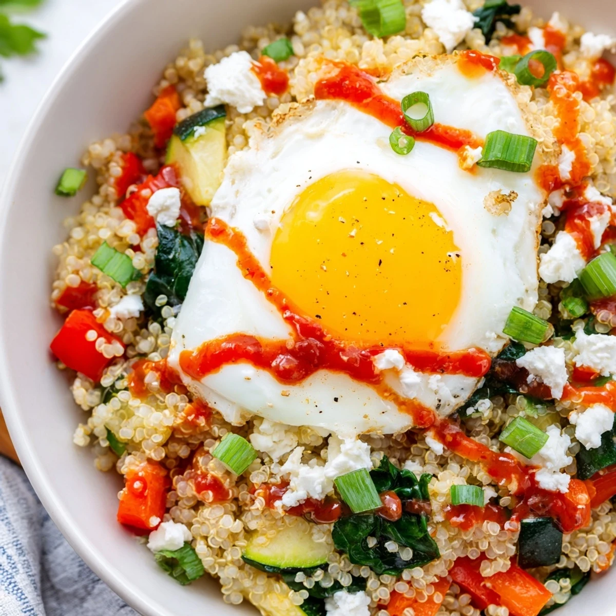 Steaming savory quinoa breakfast bowl garnished with bright parsley and a zesty sriracha drizzle