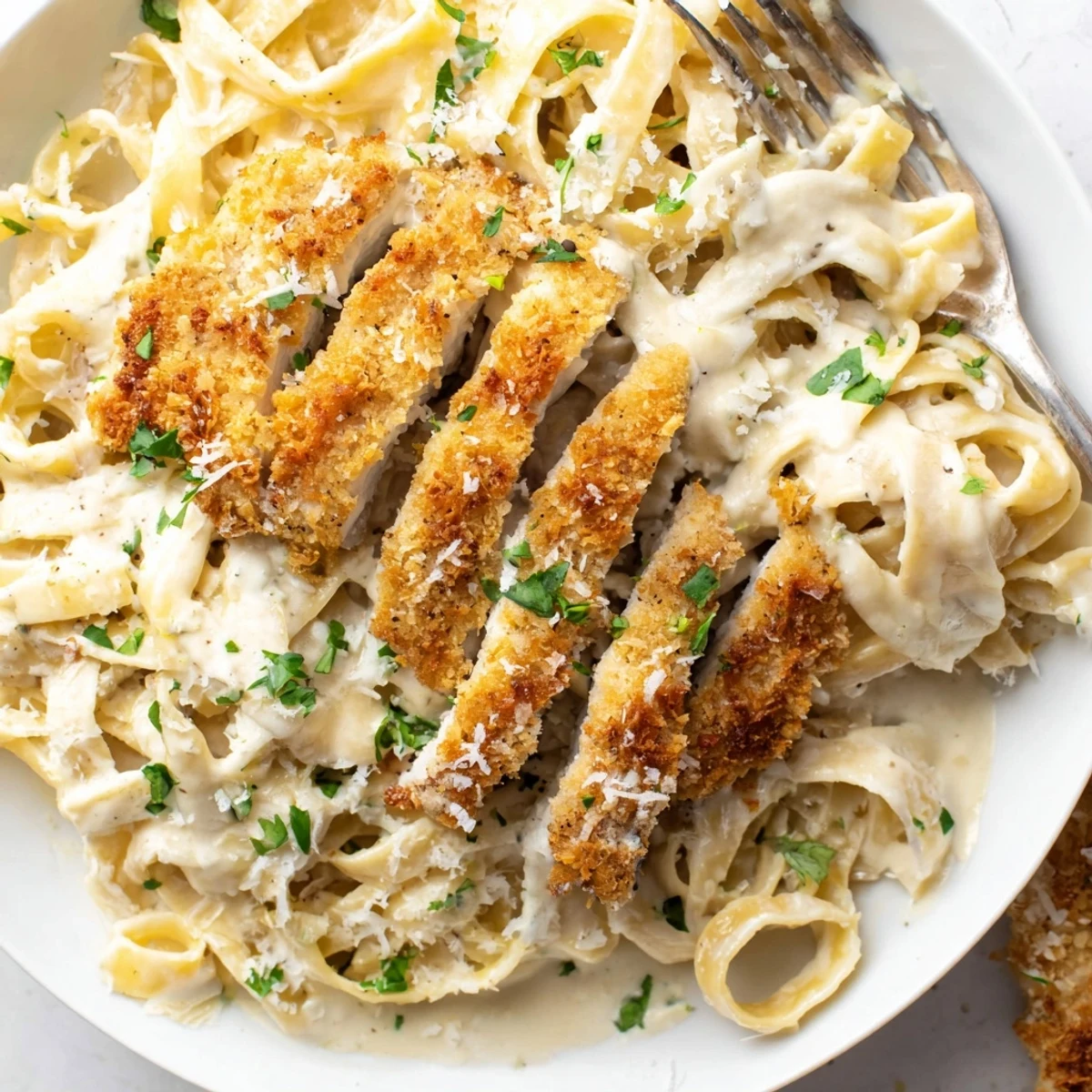 Breaded chicken cutlets resting on tender pasta drenched in homemade Alfredo sauce with parsley garnish