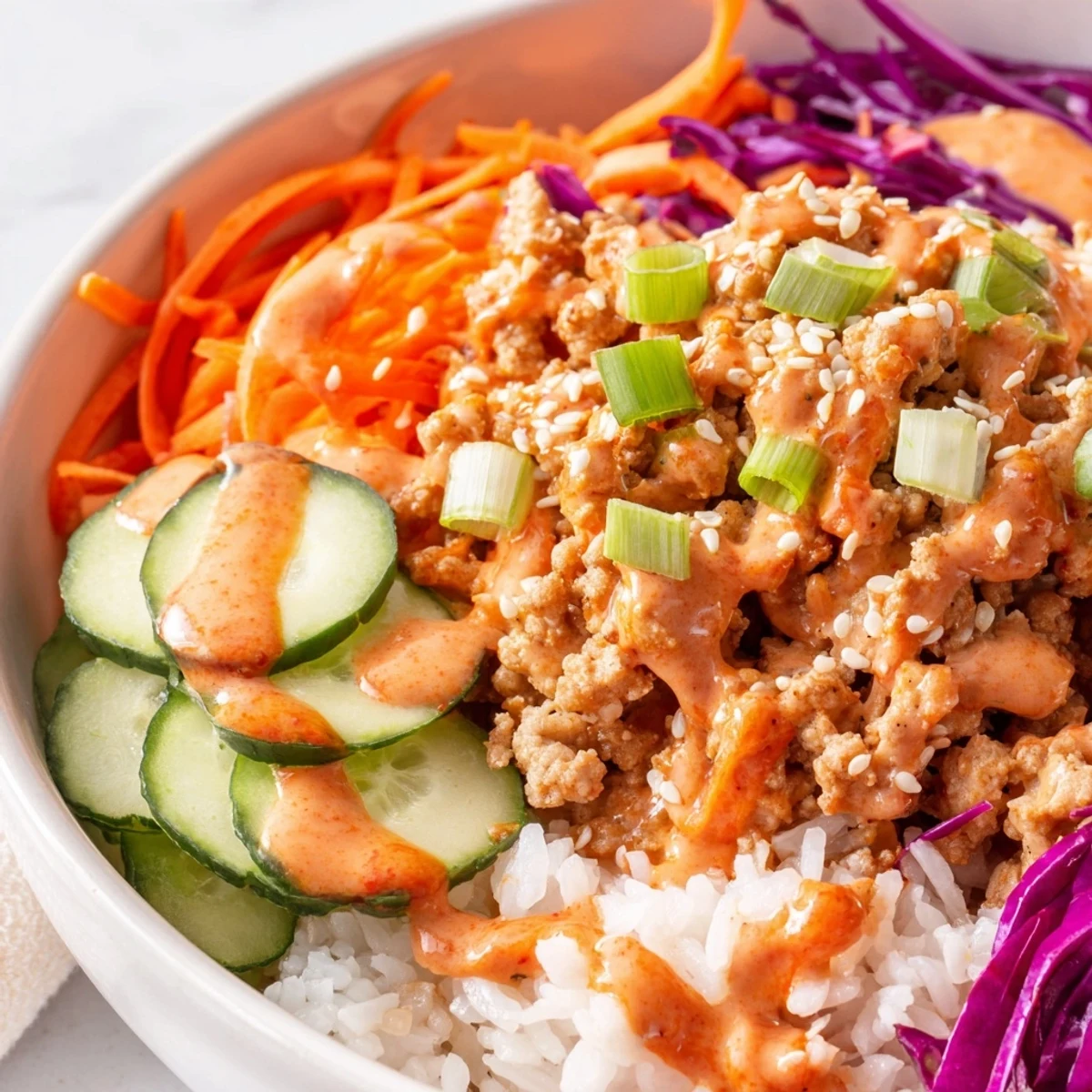 Hearty Ground Turkey Rice Bowls topped with shredded carrots, cucumber, and sweet-spicy Bang Bang Sauce
