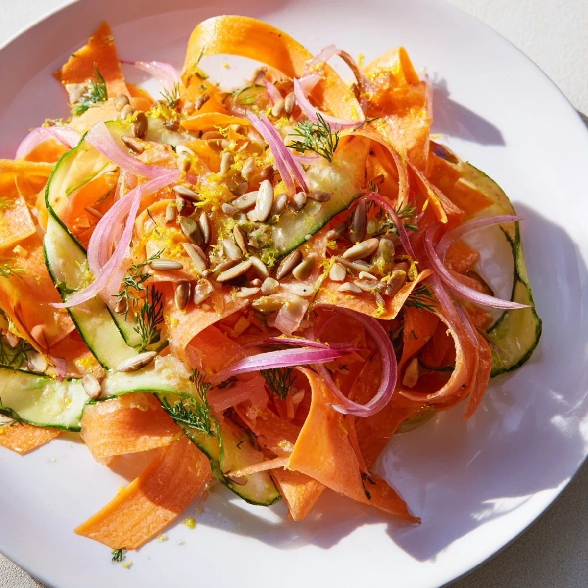 Vibrant carrot ribbon salad with cucumber slices and drizzled lemon orange dressing for a light meal.