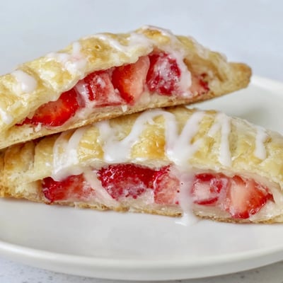 A close-up of Strawberry Hand Pies with Glaze shows flaky pastry oozing with fresh, juicy strawberry filling for a delightful dessert.