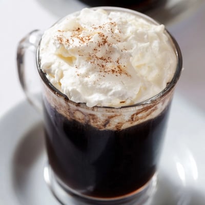 Close-up of the Irish Coffee Mocktail with Whipped Cream, highlighting the fluffy topping on rich, dark coffee in a clear glass.  