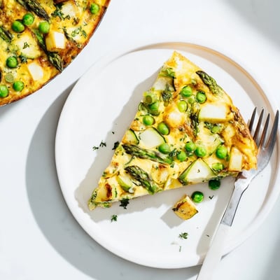 A close-up slice of Spring Vegetable Frittata with Herbs reveals fluffy eggs, melted feta, and vibrant green vegetables.  