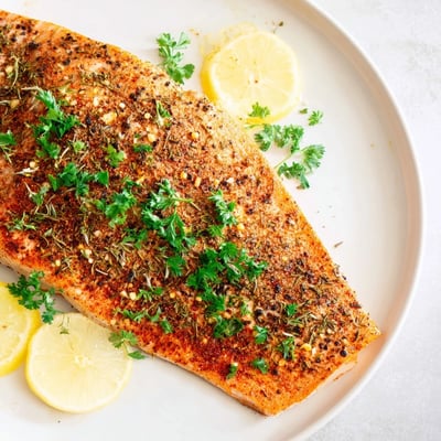 Golden baked salmon fillets glisten with olive oil, a spicy Cajun crust, and fresh parsley garnish.
